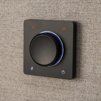 A square black smart home control panel with a central rotary knob, mounted on a textured beige fabric surface. The panel features illuminated icons for brightness, temperature, and power.