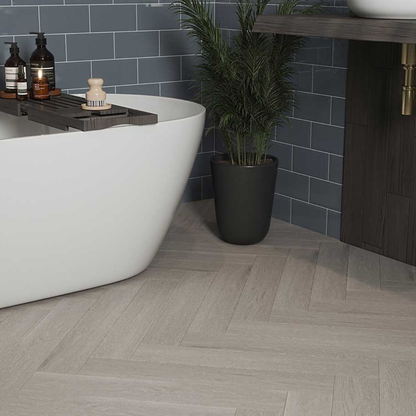 Bathroom with a white freestanding bathtub, dark tiled wall, and wooden floor.